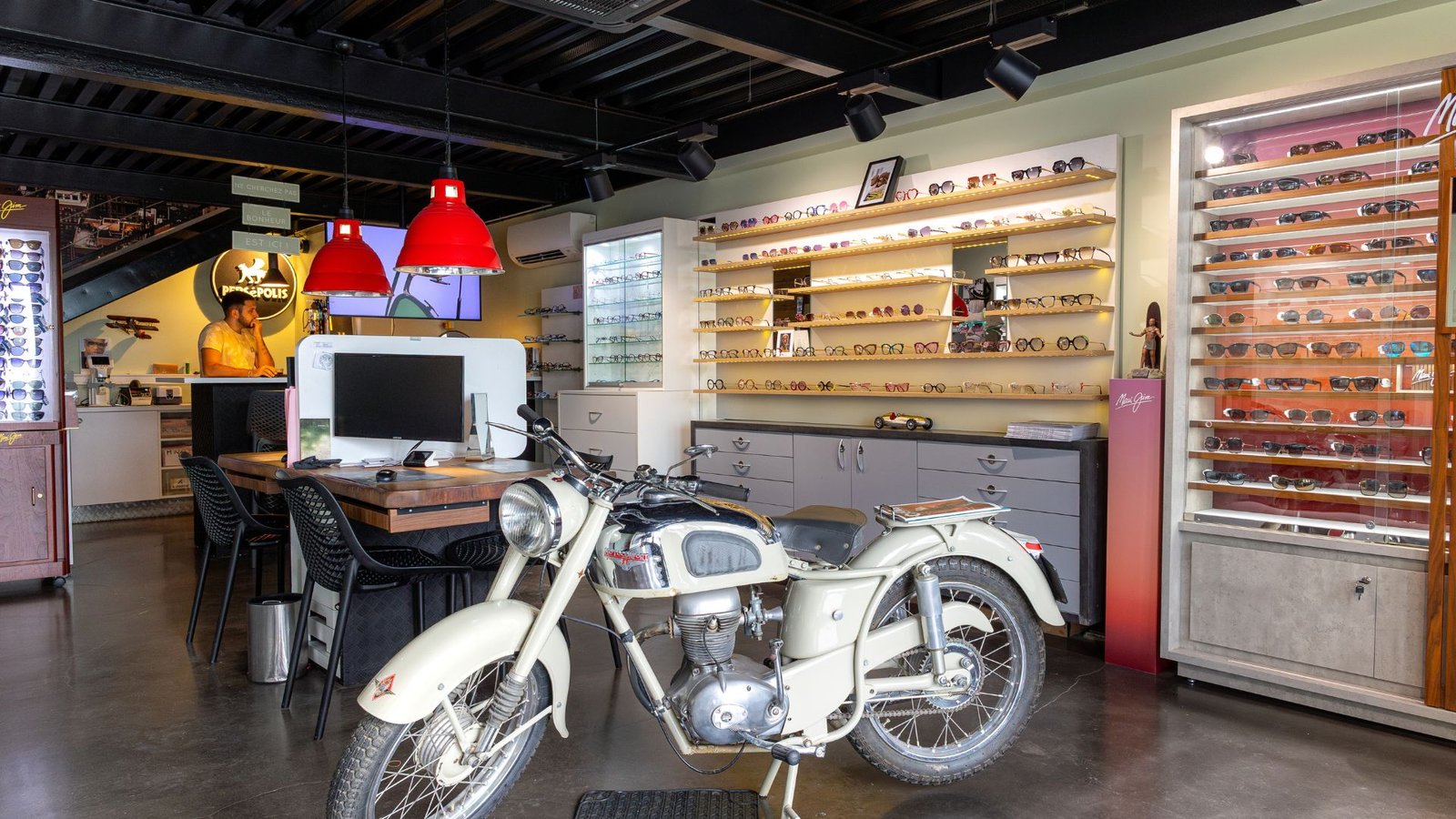Intérieur du magasin Persepolis Optique à Jarry avec présentoirs de lunettes et moto vintage en décoration
